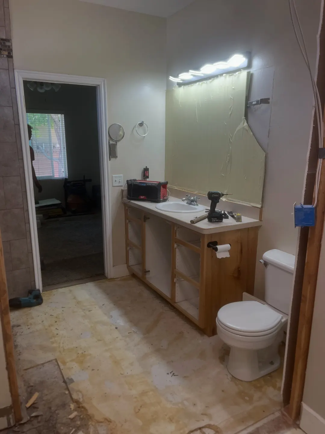 The master bathroom at tear-out: the mirror off the wall, cabinet doors and drawers pulled, flooring stripped back to the subfloor and tools out on the old counter
