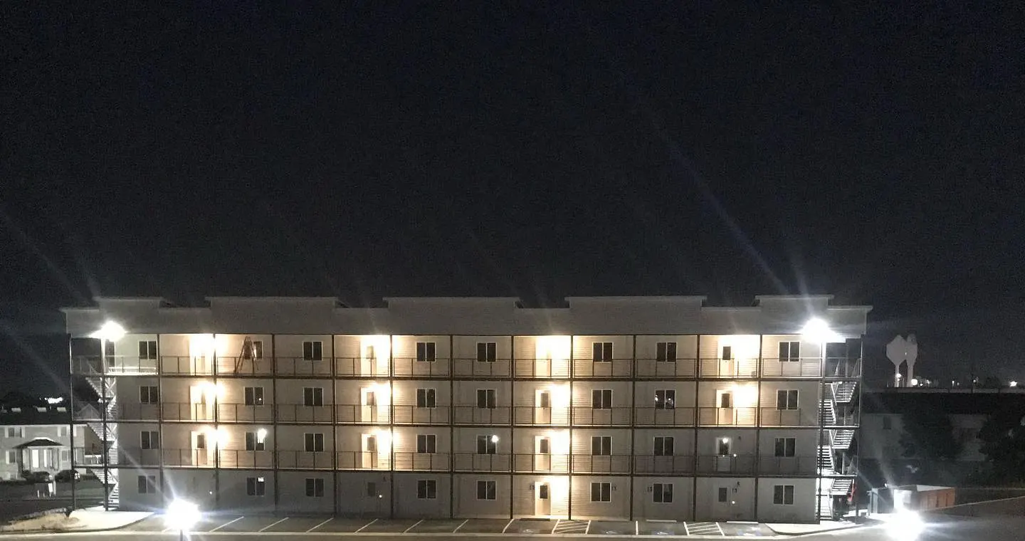 A 4-storey building Russ framed, finished and lit at night across its parking lot
