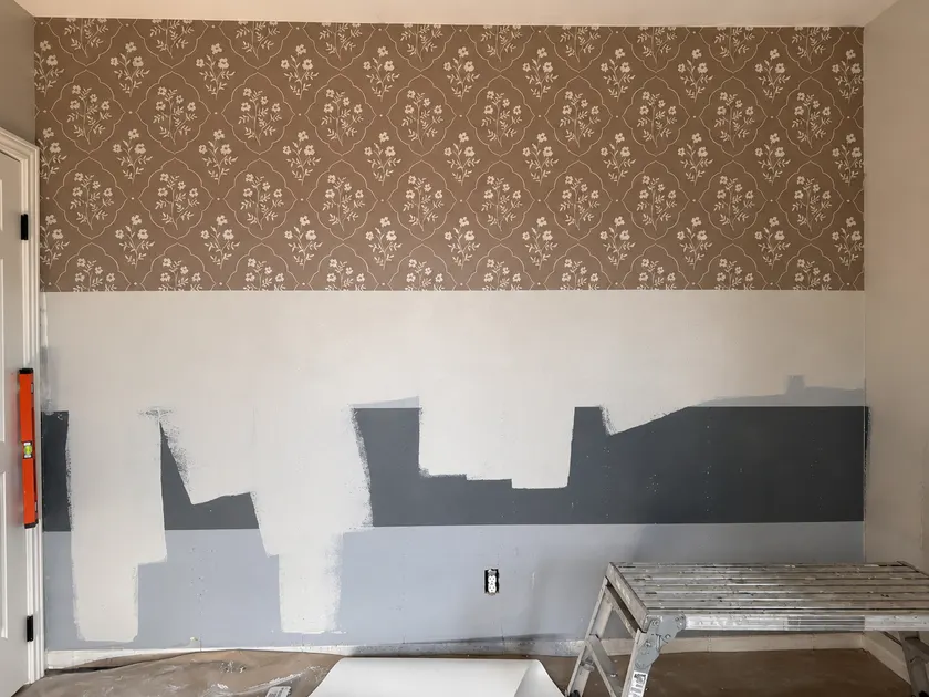 A room mid-remodel: a band of floral wallpaper still up along the top, the wall below it stripped, patched and skimmed ready for paint, with a work platform against it
