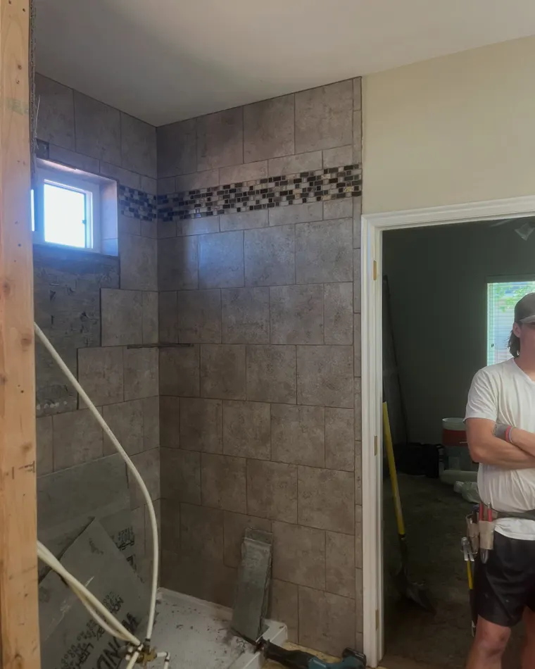 The new tiled shower: field tile set over the pan with a glass mosaic accent band and a niche cut into the wall