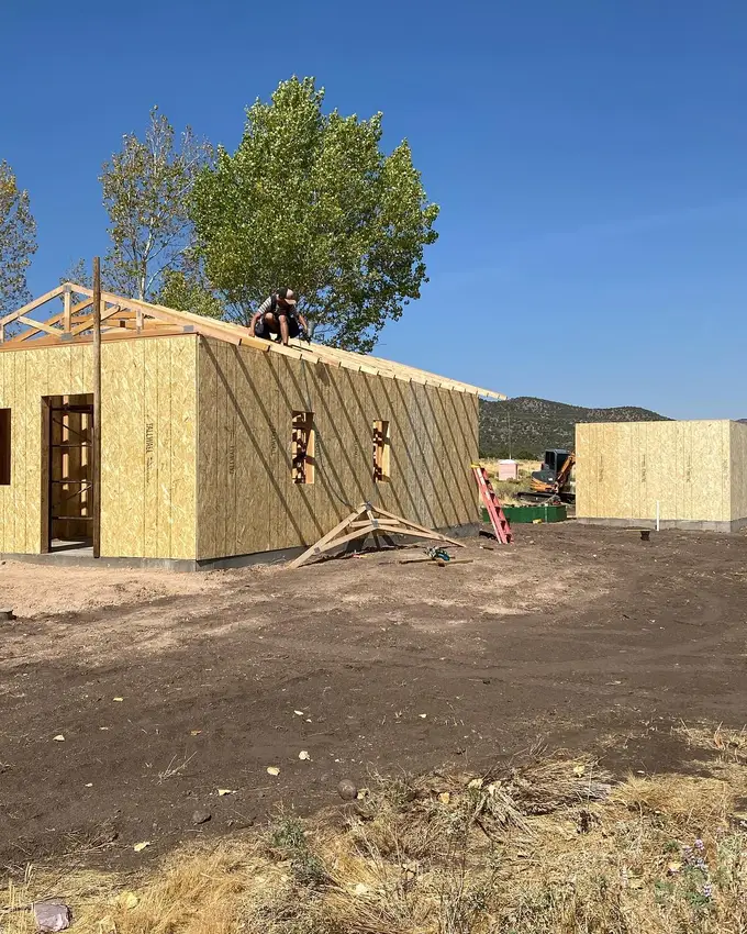 A new addition framed and sheathed, a carpenter on the ridge setting the last of the roof rafters
