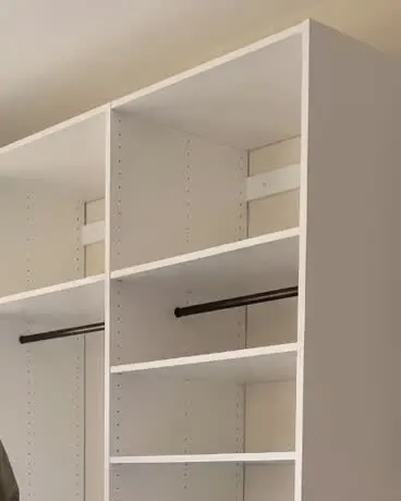 A finished built-in closet: white shelving run to the ceiling over 2 hanging rails and a bank of drawers