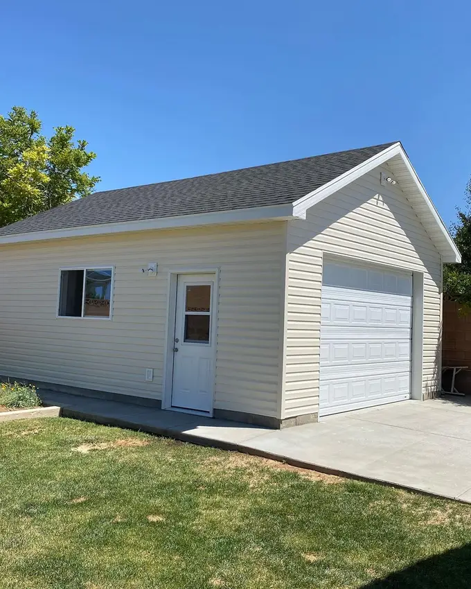 A finished detached garage on a new slab: vinyl siding, a service door and window, lawn run up to the apron