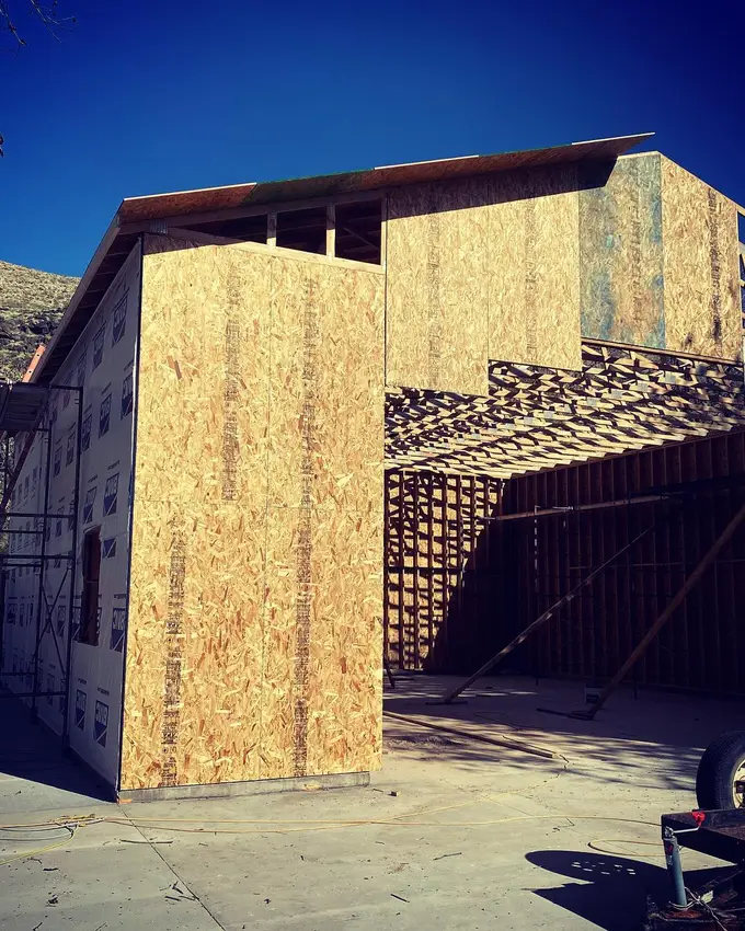 A carpenter guiding a roof truss off a flatbed under a crane hook on a Cedar City job