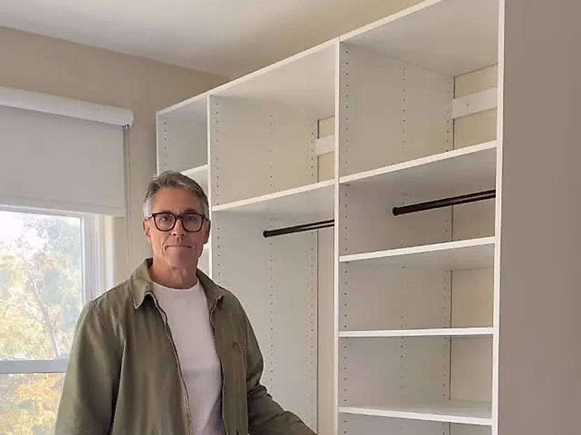 A finished walk-in closet built in white melamine, with adjustable shelving, 2 hanging rails and a bank of drawers