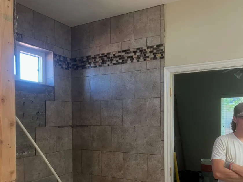 A new tiled shower being installed with a glass mosaic accent band